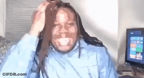 A Man With Dreadlocks Is Sitting In Front Of A Computer And Holding His Hair . GIF