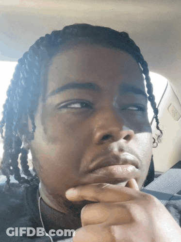 A Man With Dreadlocks Is Sitting In The Back Seat Of A Car With His Hand On His Chin GIF