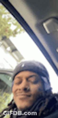 A Man With Dreadlocks Is Sitting In The Driver 'S Seat Of A Car And Smiling . GIF
