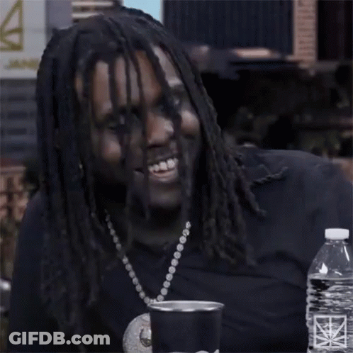 A Man With Dreadlocks Is Smiling While Sitting At A Table With A Bottle Of Water GIF