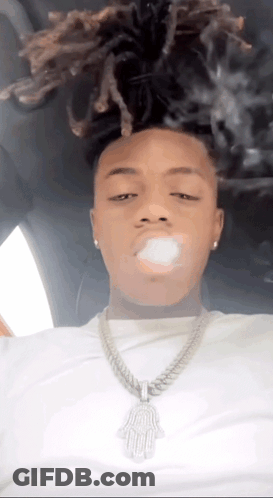A Man With Dreadlocks Is Smoking A Cigarette In A Car While Wearing A Necklace . GIF