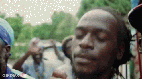A Man With Dreadlocks Is Smoking A Cigarette In Front Of A Crowd Of People With Their Eyes Closed . GIF