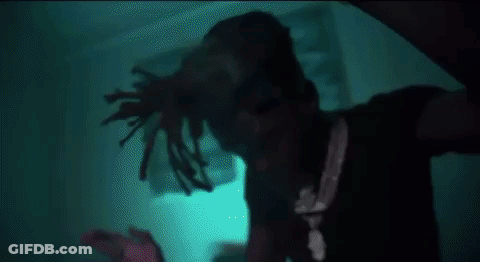 A Man With Dreadlocks Is Standing In A Dark Room In Front Of A Blue Light . GIF