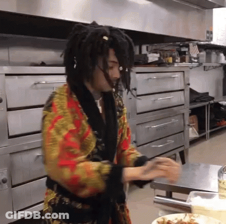 A Man With Dreadlocks Is Standing In A Kitchen In Front Of An Oven . GIF
