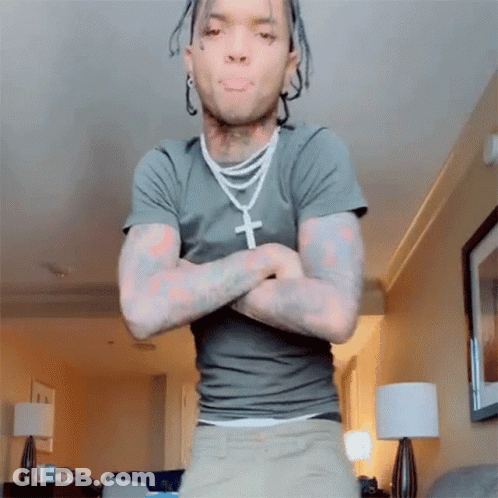 A Man With Dreadlocks Is Standing In A Living Room With His Arms Crossed GIF
