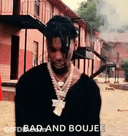 A Man With Dreadlocks Is Standing In Front Of A Brick Building . GIF