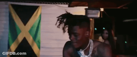 A Man With Dreadlocks Is Standing In Front Of A Flag . GIF