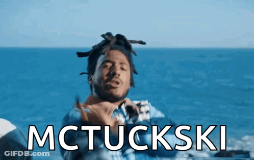 A Man With Dreadlocks Is Standing In Front Of The Ocean And The Words Mctuckski Are Displayed Above Him GIF