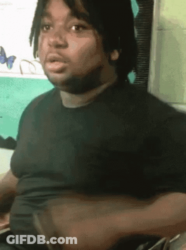 A Man With Dreadlocks Is Wearing A Black Shirt And Making A Face GIF