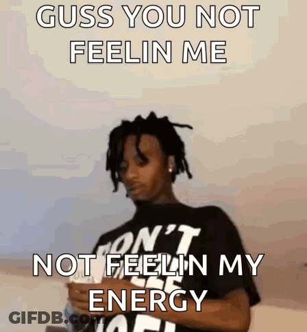 A Man With Dreadlocks Is Wearing A Black Shirt That Says ' Guss You Not Feelin Me ' On It . GIF