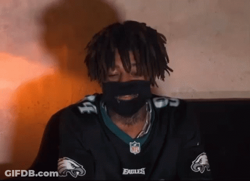 A Man With Dreadlocks Is Wearing A Eagles Jersey And A Mask . GIF