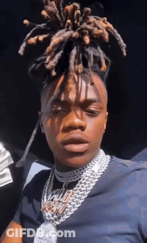 A Man With Dreadlocks Is Wearing A Necklace That Says ' King ' On It . GIF