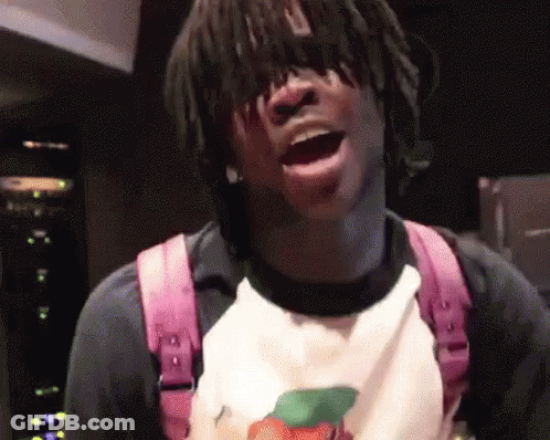 A Man With Dreadlocks Is Wearing A Pink Backpack And A White Shirt With A Peach On It . GIF
