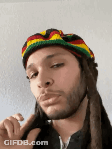 A Man With Dreadlocks Is Wearing A Rasta Hat And Making A Funny Face . GIF