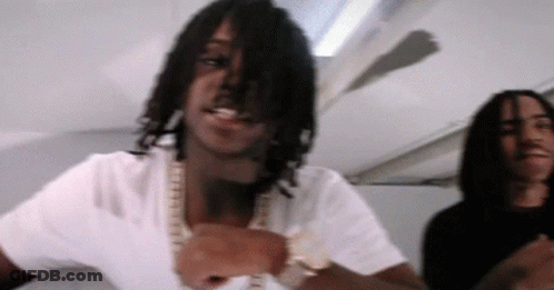 A Man With Dreadlocks Is Wearing A White Shirt And Gold Chains GIF
