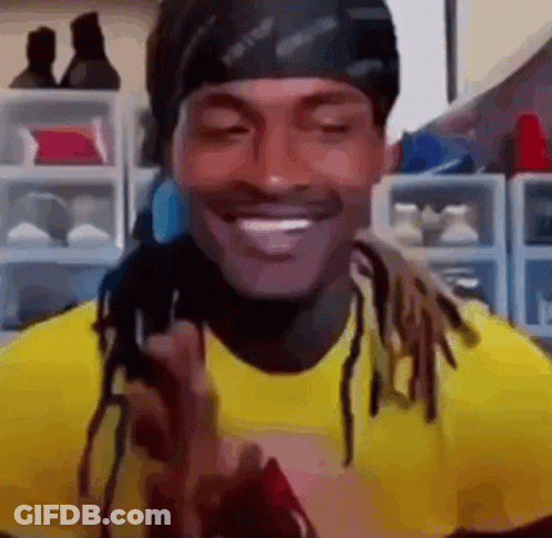A Man With Dreadlocks Is Wearing A Yellow Shirt And A Black Headband And Smiling . GIF