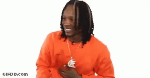 A Man With Dreadlocks Is Wearing An Orange Sweater And A Necklace With A Pendant . GIF