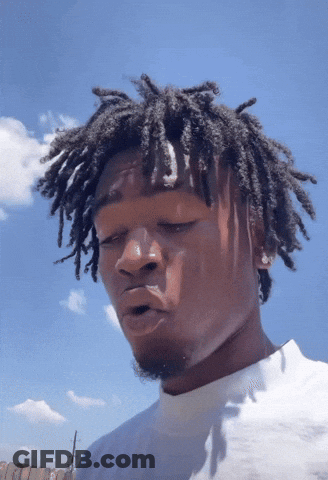 A Man With Dreadlocks Looks At The Camera With A Blue Sky Behind Him GIF