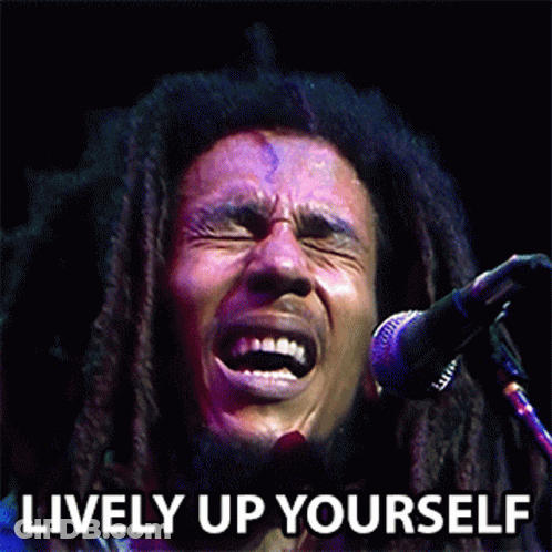 A Man With Dreadlocks Singing Into A Microphone With The Words Lively Up Yourself Behind Him GIF