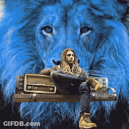 A Man With Dreadlocks Sits On A Bench With A Lion Behind Him GIF