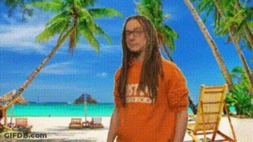 A Man With Dreadlocks Wearing An Orange Shirt With The Number 57 On It Stands On A Beach GIF