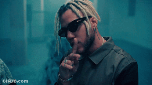 A Man With Dreadlocks Wearing Sunglasses Has His Finger On His Mouth GIF