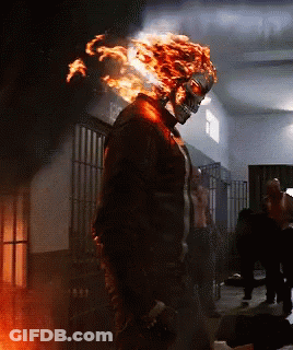 A Man With Flames Coming Out Of His Head Is Standing In A Dark Room GIF
