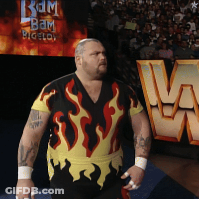 A Man With Flames On His Shirt Is Standing In Front Of A Sign That Says Bam Bigelow GIF
