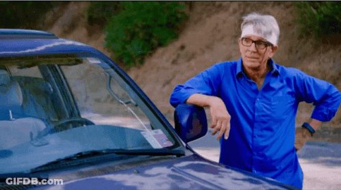 A Man With Glasses And A Bandage On His Head Leans On A Car GIF