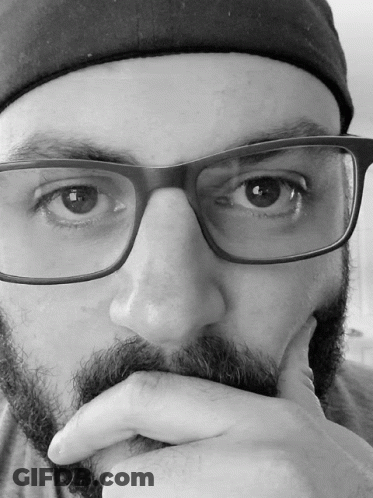 A Man With Glasses And A Beard Holds His Hand To His Face GIF