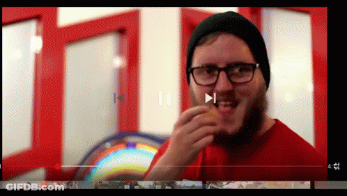 A Man With Glasses And A Beard Is Eating A Burger GIF