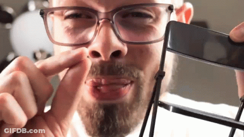 A Man With Glasses And A Beard Is Holding A Black Object In Front Of His Face GIF