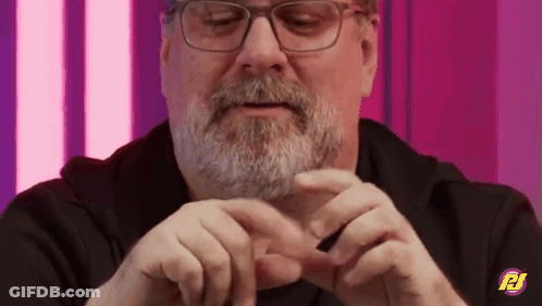 A Man With Glasses And A Beard Is Holding Something In His Hands And Making A Heart Shape With His Hands . GIF
