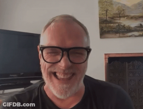 A Man With Glasses And A Beard Is Laughing In Front Of A Panasonic Television GIF