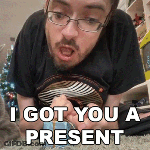 A Man With Glasses And A Beard Is Laying On The Floor And Says I Got You A Present In White GIF