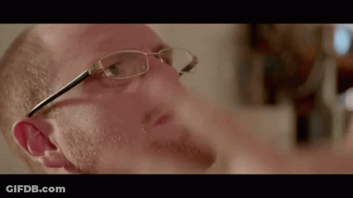 A Man With Glasses And A Beard Is Looking Down At Something GIF
