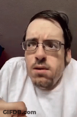 A Man With Glasses And A Beard Is Making A Funny Face While Wearing A White Shirt . GIF