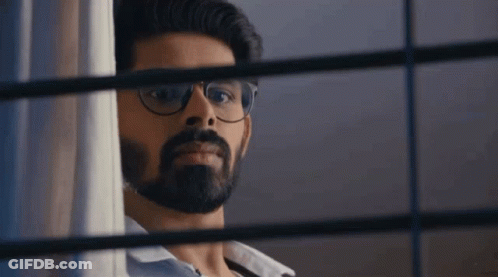 A Man With Glasses And A Beard Is Peeking Out Of A Window . GIF