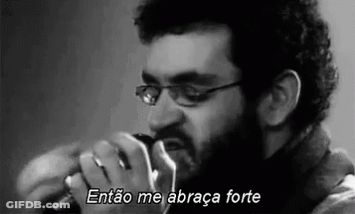 A Man With Glasses And A Beard Is Singing Into A Microphone . GIF
