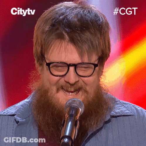 A Man With Glasses And A Beard Is Singing Into A Microphone With The Hashtag #Cgt GIF