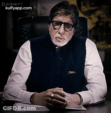A Man With Glasses And A Beard Is Sitting At A Desk . GIF