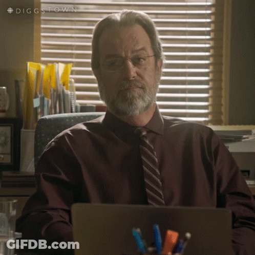 A Man With Glasses And A Beard Is Sitting At A Desk With A Laptop In Front Of Him GIF