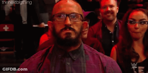 A Man With Glasses And A Beard Is Sitting In A Crowd With A Sign That Says Neville . GIF