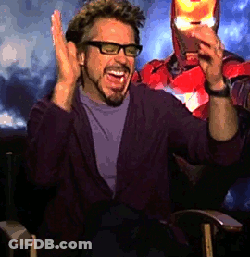 A Man With Glasses And A Beard Is Sitting In Front Of A Man In A Superhero Costume GIF
