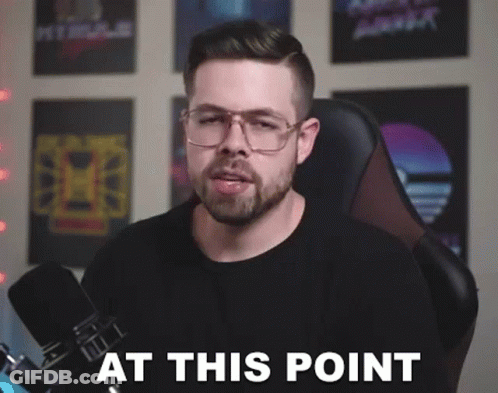 A Man With Glasses And A Beard Is Sitting In Front Of A Microphone With The Words At This Point . GIF