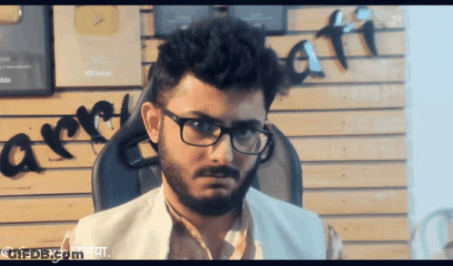 Man With Glasses And Beard Sitting By Arre Wall GIF