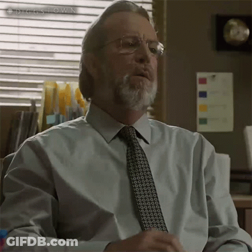A Man With Glasses And A Beard Is Sitting In Front Of A Window With A Sign That Says #Diggstown On It GIF