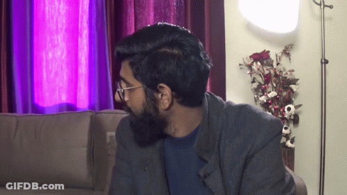 A Man With Glasses And A Beard Is Sitting On A Couch In A Living Room GIF