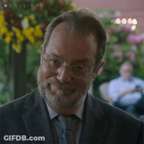 A Man With Glasses And A Beard Is Smiling And Looking At The Camera . GIF