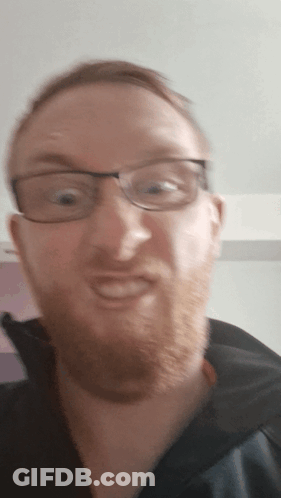 A Man With Glasses And A Beard Is Smiling For The Camera GIF